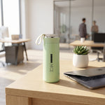 Green insulated bottle on a desk in an office setting with a laptop and plant.